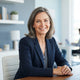 A smiling woman in a professional, bright office setting with slate blue and white accents representing a satisfied customer.